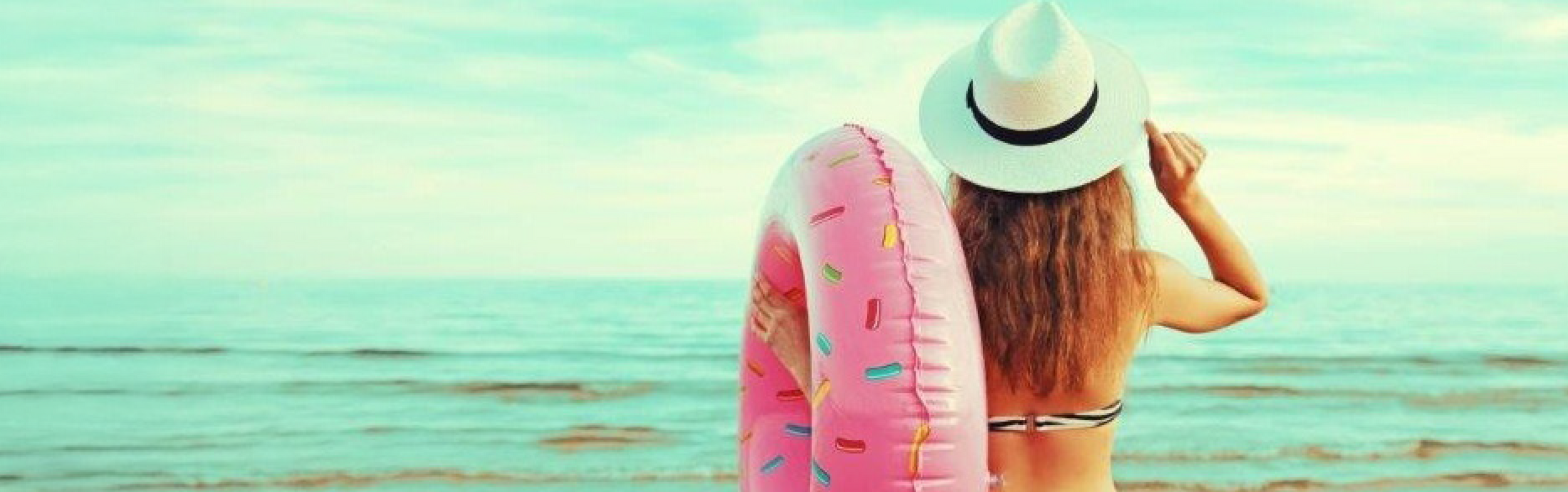 Eine junge Frau schaut auf das offene Meer und hält einen großen Schwimmreifen im Arm.