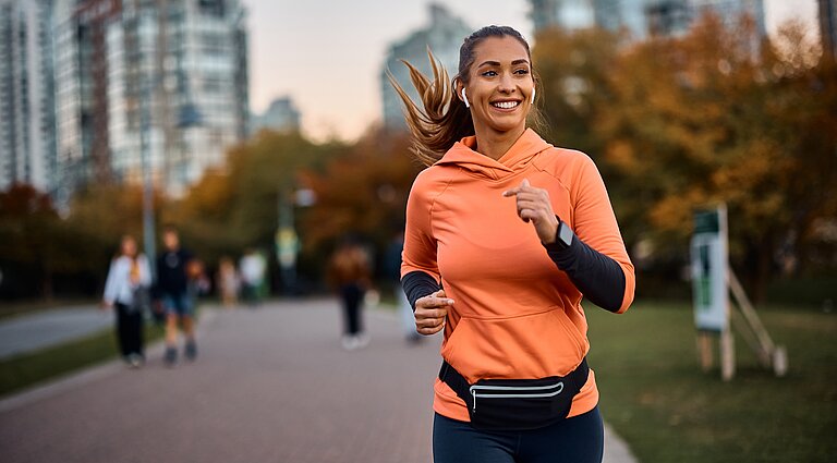 Frau joggt durch einen Park und lächelt.